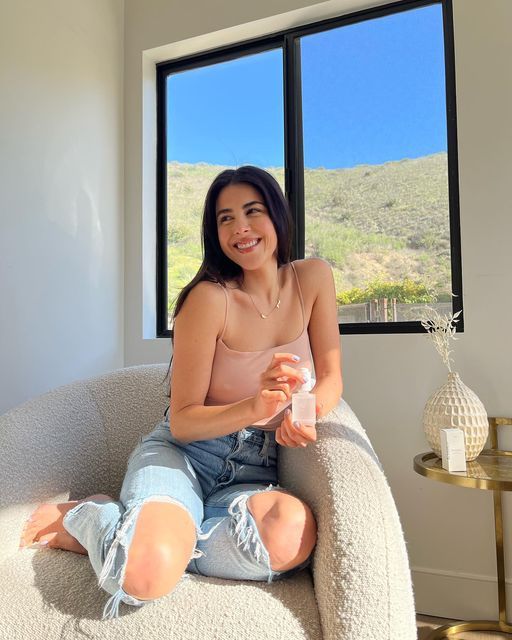 a woman sitting on a chair with a bottle in her hand and smiling at the camera