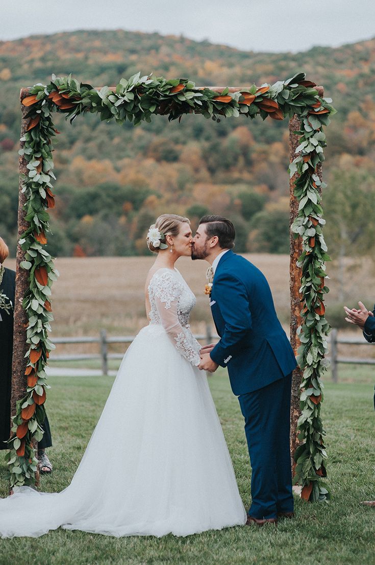 a bride and groom kissing under an arch decorated with greenery at their wedding ceremony