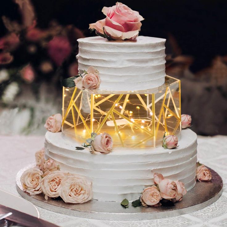 a white wedding cake with pink roses on the side and an illuminated sign that says love