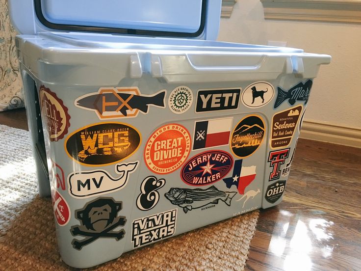 a cooler with many stickers on it sitting on the floor next to a rug