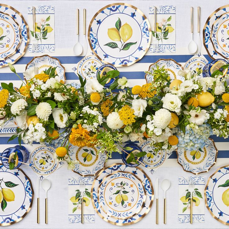 the table is set with plates, flowers and lemons in blue and white dishes