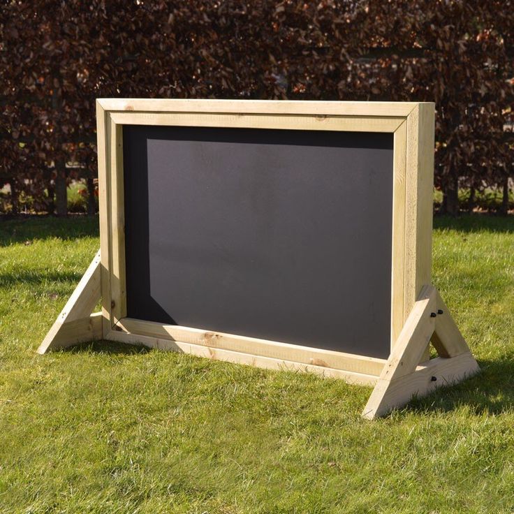 a chalkboard sitting in the grass next to a wooden frame on top of it