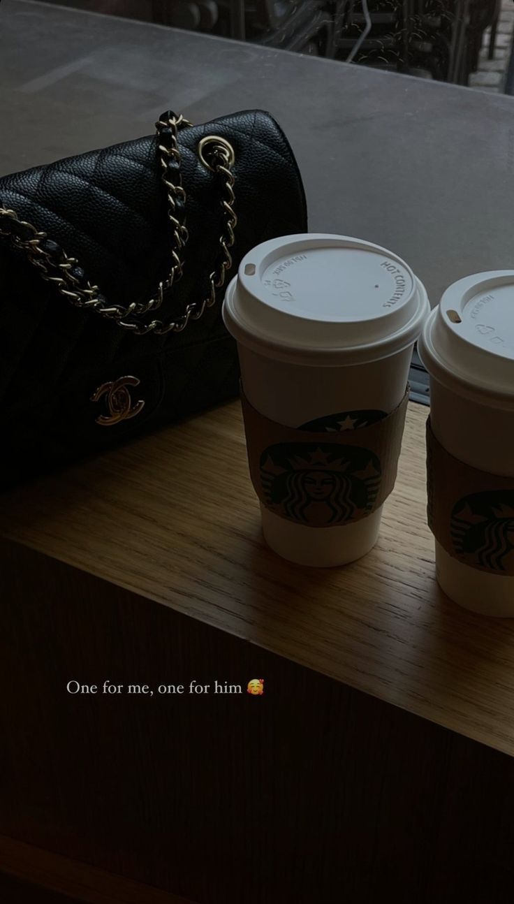 two cups of coffee sitting on top of a wooden table next to a handbag