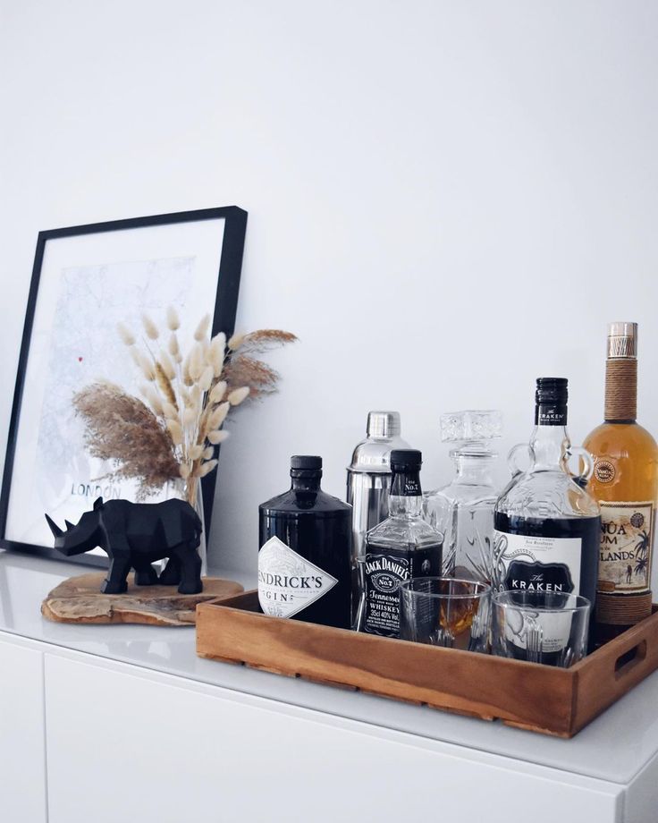 a wooden tray filled with liquor bottles on top of a white counter next to a framed photograph