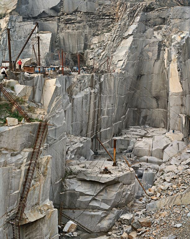 people are standing on the side of a mountain with many large rocks and ladders