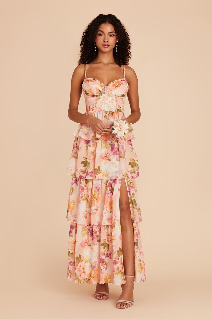 a woman wearing a pink floral print dress with high slit and side slit, standing in front of a beige background