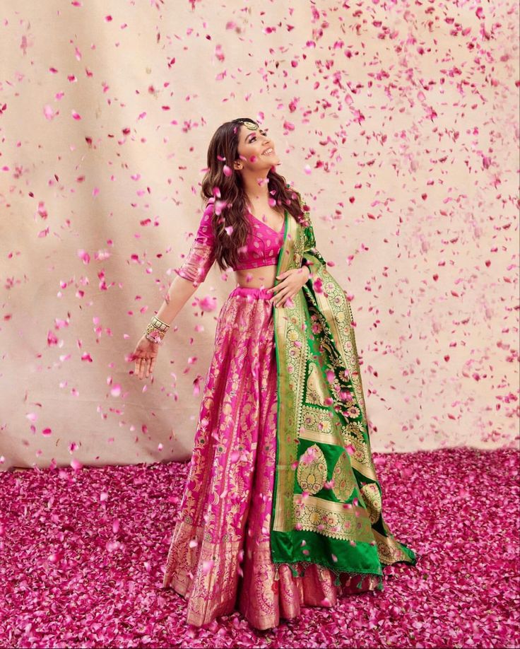 a woman in a pink and green lehenga with petals falling down on her