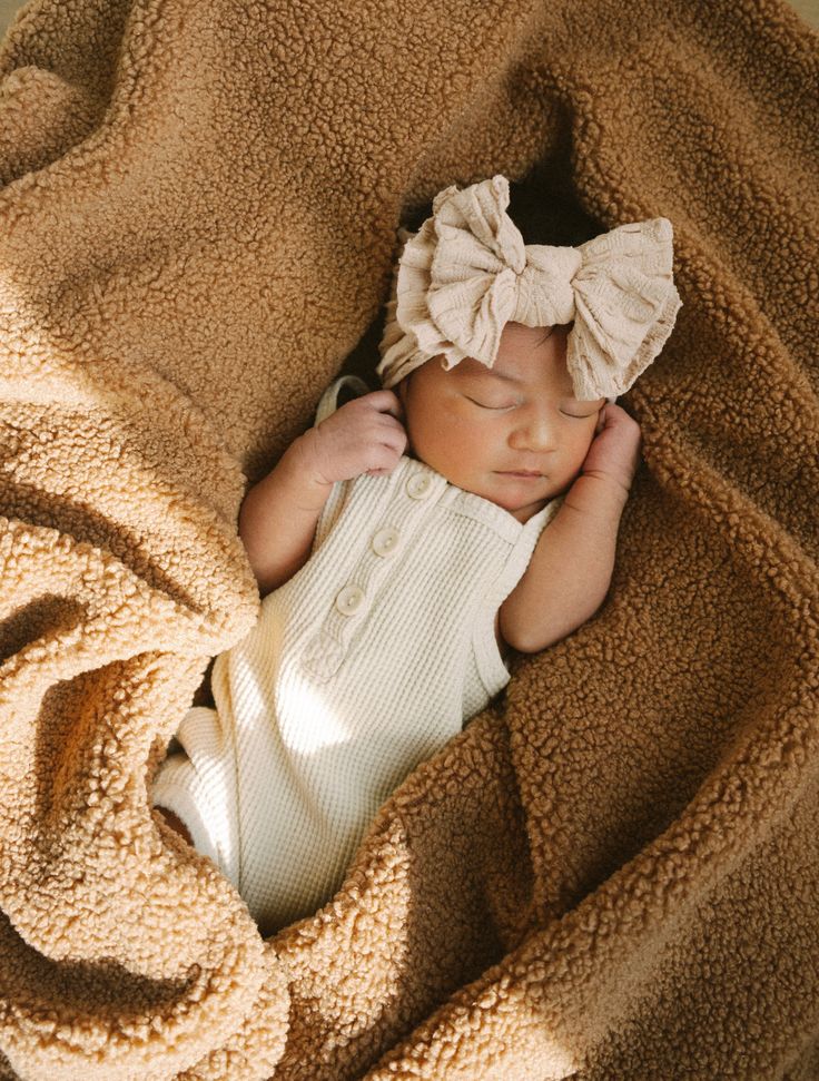 a newborn baby is wrapped in a blanket and wearing a headband with a bow