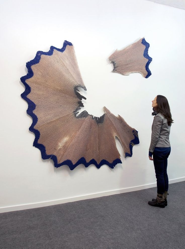 a woman standing in front of a wall with an art piece hanging on it's side