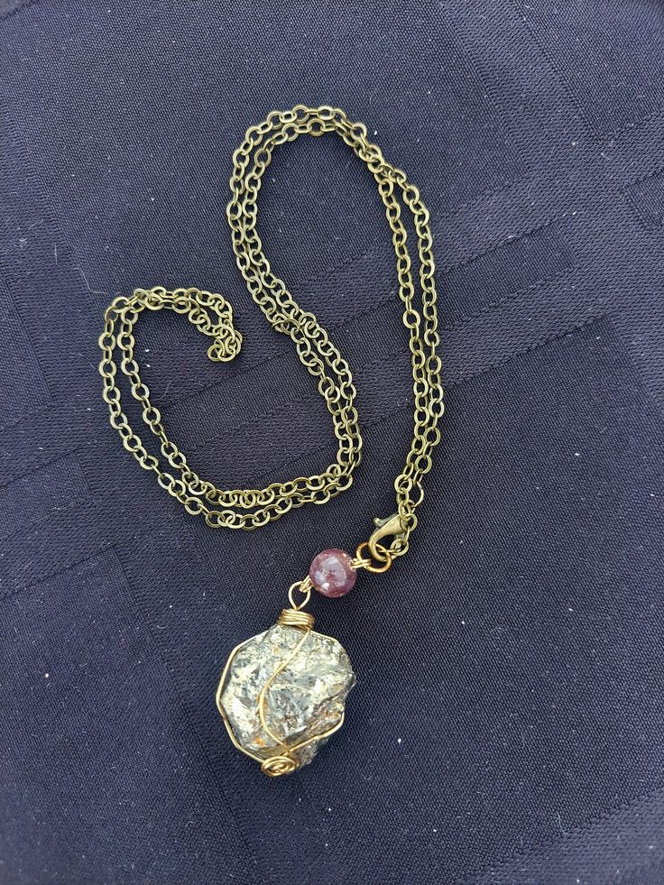 Pyrite stone from Perú, wrapped in gold plated wire, hangs from an 22-inch patinated brass chain that clasps in front. A purple lepidolite bead complements the golden color. This piece is great for honoring the Sun! It can also be used as a meditation/divination pendulum thanks to the weight and swing of the stone and front clasping. Handmade Copper Wire Gold Necklace, Handmade Gold Copper Wire Necklace, Handmade Gold Necklace With Copper Wire, Spiritual Gold Crystal Necklaces, Gold Amethyst Round Pendant Jewelry, Handmade Gold Crystal Metal Necklace, Gold Necklace With Copper Wire As Gift, Wire Wrapped Amethyst Necklaces For Meditation, Gold Spiritual Crystal Necklaces Nickel Free