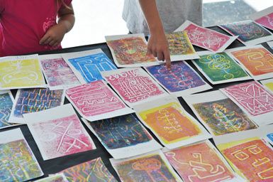 children looking at art work on display in an open air market area with people standing around