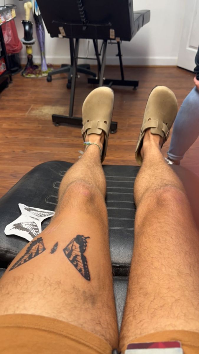 a man's legs with tattoos sitting on top of a piece of luggage in a room