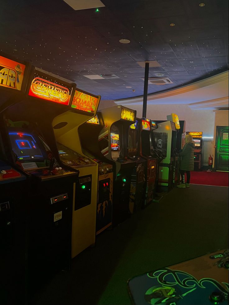 several video game machines lined up in a room with green carpet and lights on the ceiling