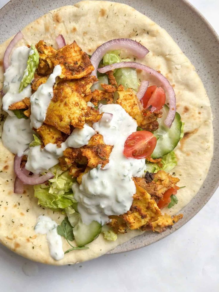 a taco with chicken, lettuce and tomatoes on it sitting on a plate