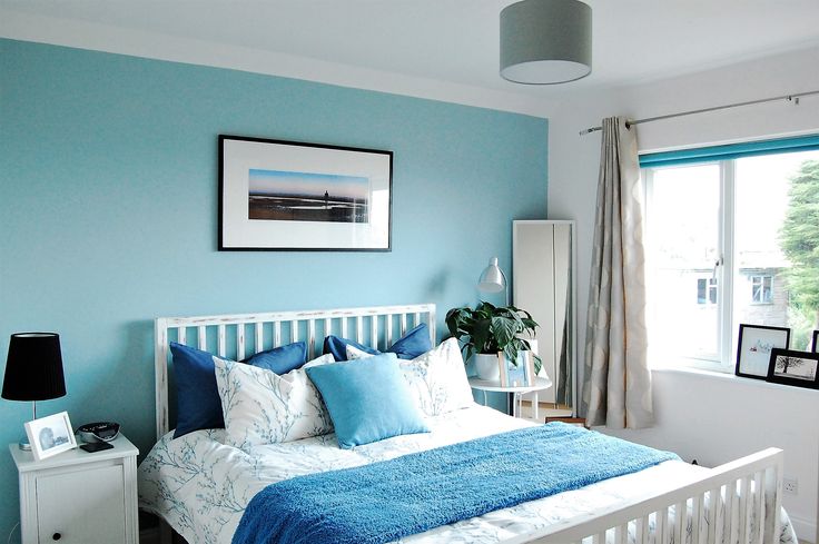 a bedroom with blue walls and white bedding in front of a large window on the side