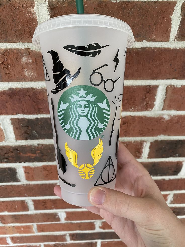 a hand holding up a starbucks cup with harry potter symbols on it and a green straw