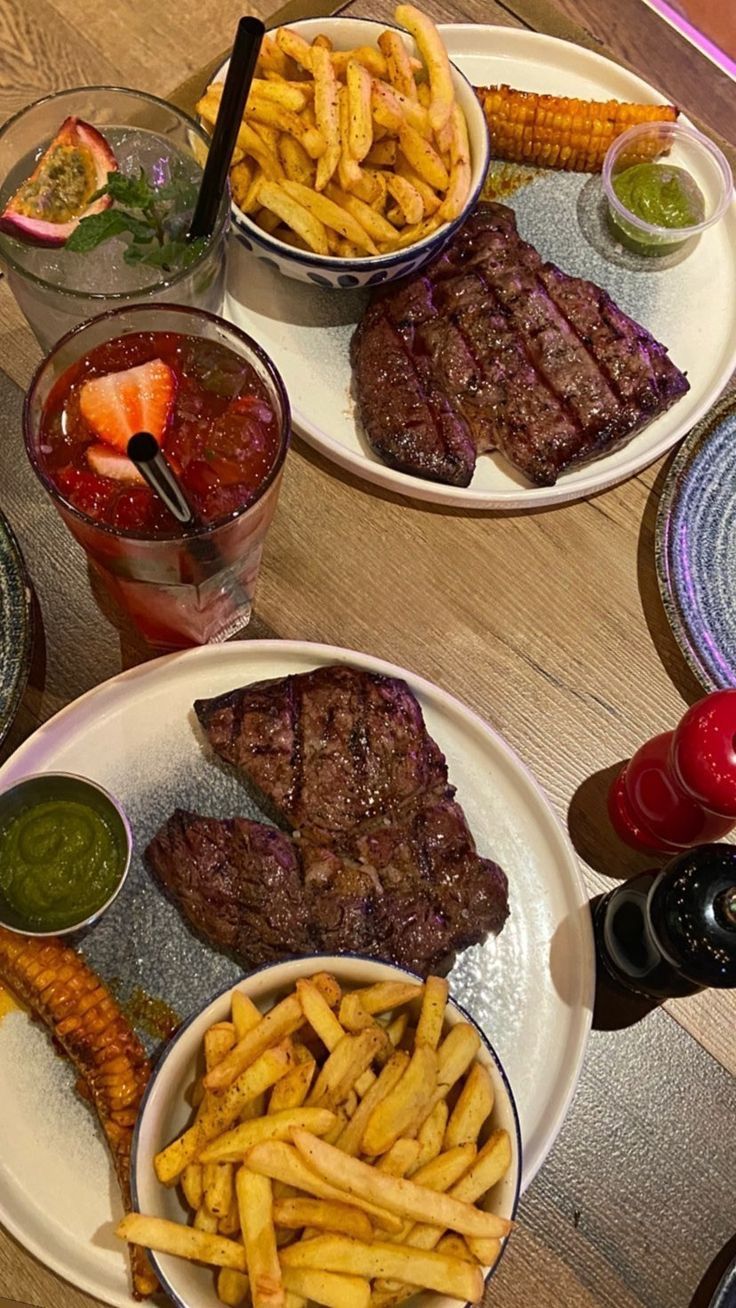 three plates with steak, french fries and fruit on them sitting on a wooden table