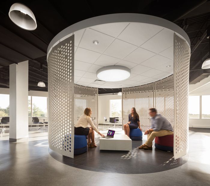 three people are sitting in an office with round seating and white partitions on the walls