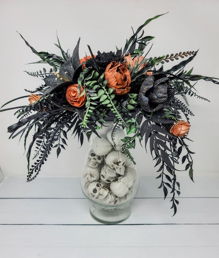 an arrangement of flowers in a vase with rocks and leaves on the table next to it