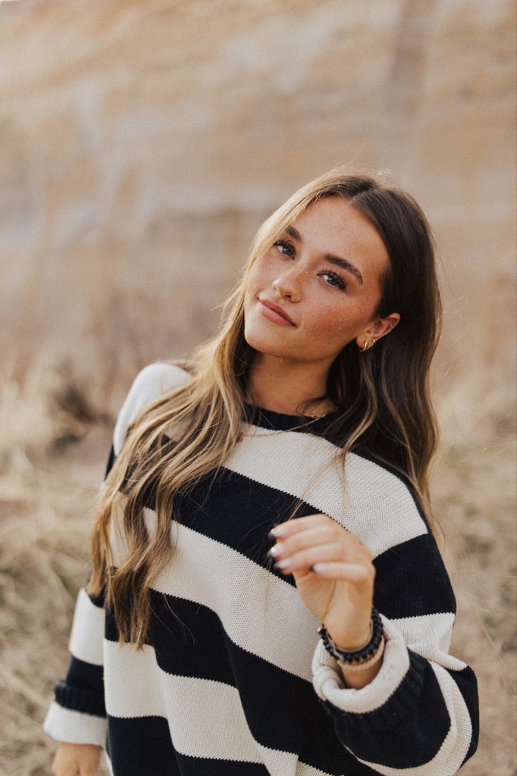 a woman wearing a black and white striped sweater standing in the desert with her hand on her hip