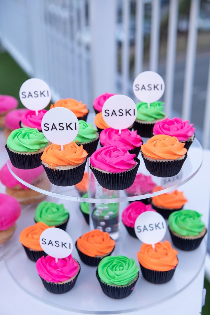 cupcakes with different colored frosting sitting on a cake stand that says saski