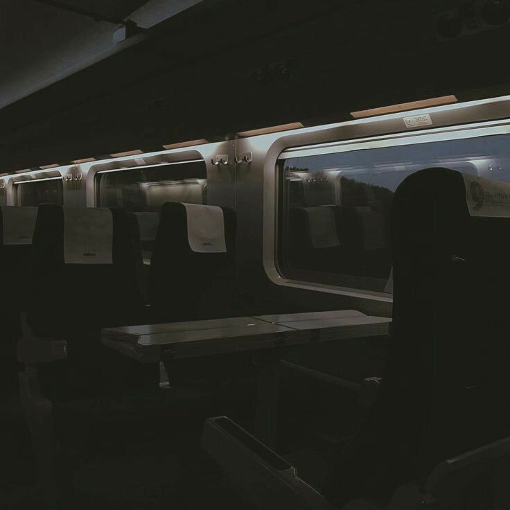 the interior of a subway train with empty seats and tables on each side, at night