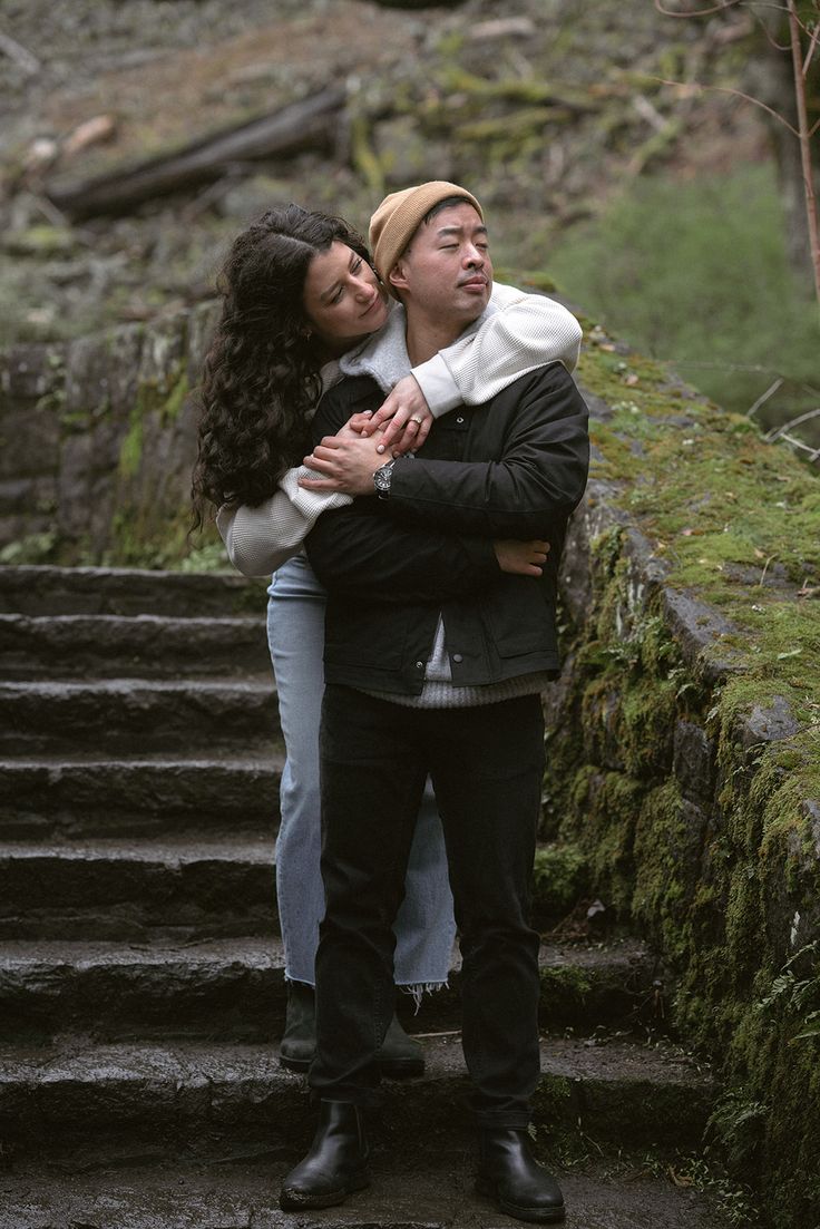 a man and woman embracing each other on the steps in front of some mossy trees