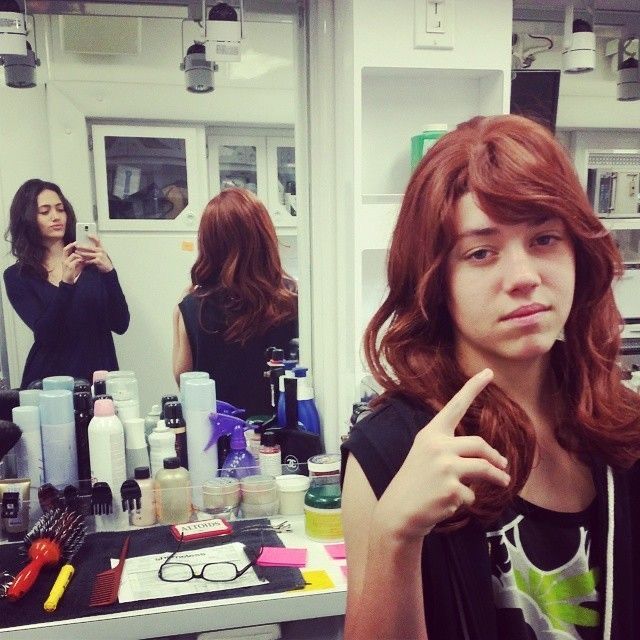 a woman with red hair in front of a mirror pointing to the side while another woman stands behind her