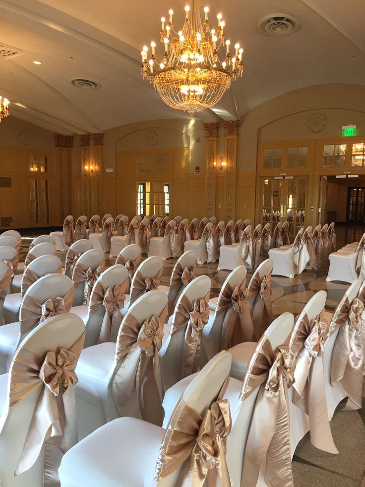 rows of chairs with bows on them and chandelier hanging from the ceiling in an elegant ballroom