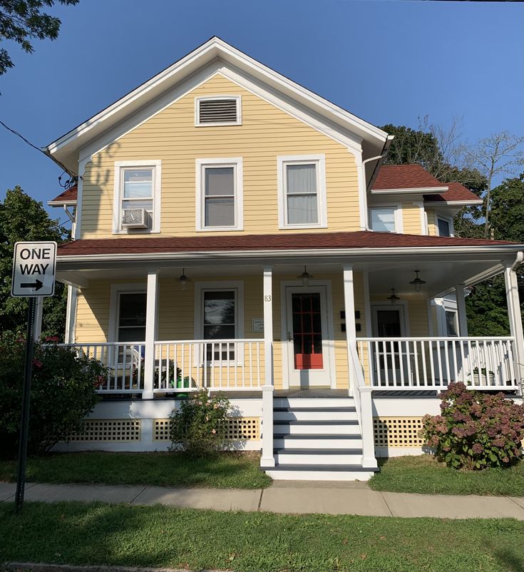 a yellow two story house with white porches and red roof on a sunny day