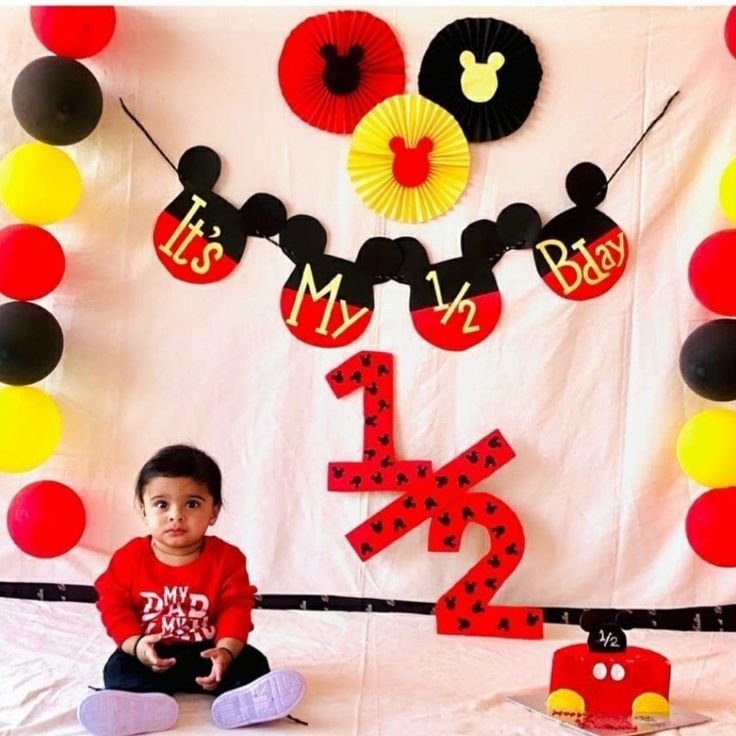 a little boy sitting on the floor in front of a mickey mouse cake and decorations