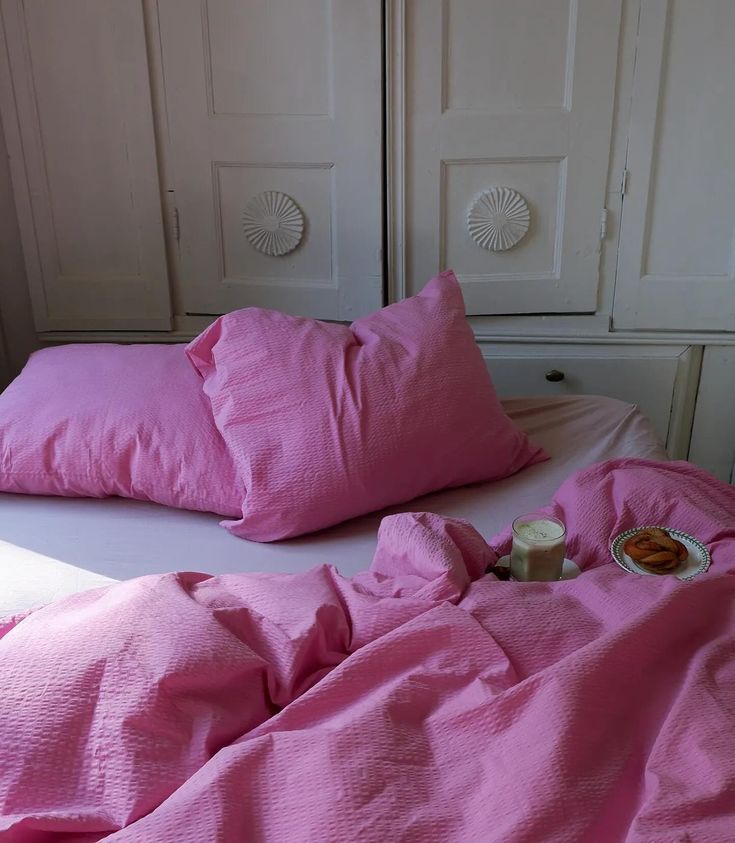 a bed covered in pink sheets and pillows with food on the bottom of each pillow