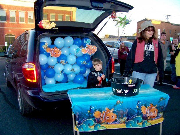 a woman standing next to a little boy in front of a car trunk filled with balloons