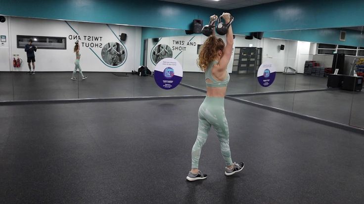 a woman is doing exercises in the gym with kettles on her head and arms