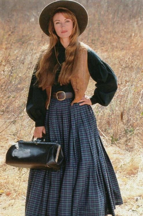 a woman in a long dress and hat poses for the camera with her hand on her hip