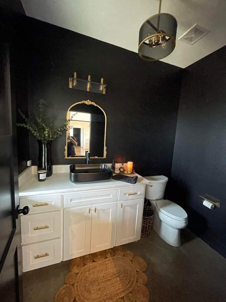 a bathroom with black walls, white cabinets and a gold mirror on the wall above the sink