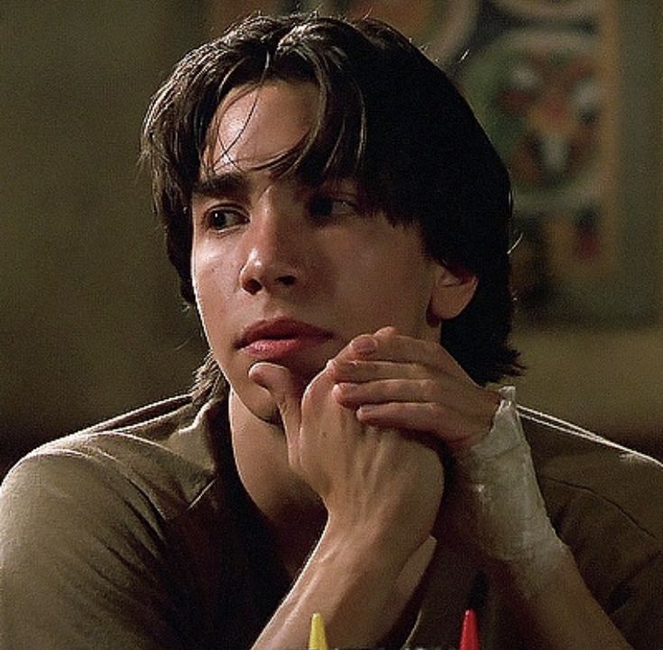 a young man sitting at a table with crayons in front of his face