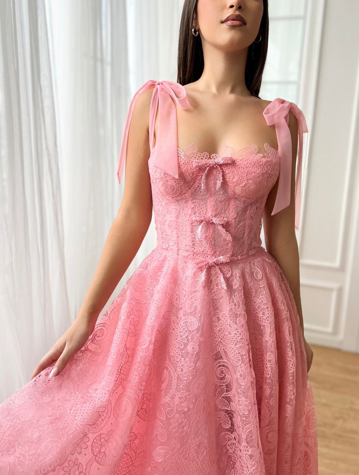 Step into spring celebrations with an air of enchantment in this exquisite midi-length dress, rendered in a delicate rose pink hue that whispers romance. Its bustier top, adorned with a trio of charming bow embellishments, features built-in pads and boning to sculpt and define your silhouette. Crafted from the finest Leavers lace and tulle fabric, it promises a touch of timeless elegance and texture. The dress cinches at the waist before flowing into a graceful midi-length style, complete with i Pink Lace Corset Dress For Prom, Pink Sleeveless Corset Dress For Wedding, Pink Sleeveless Wedding Corset Dress, Pink Corset Dress With Lined Bodice For Wedding, Pink Corset Wedding Dress With Lined Bodice, Pink Wedding Corset Dress With Lined Bodice, Pink Sleeveless Evening Dress With Boned Bodice, Pink Dress With Lace Bodice And Spaghetti Straps, Pink Lace Corset Dress For Wedding