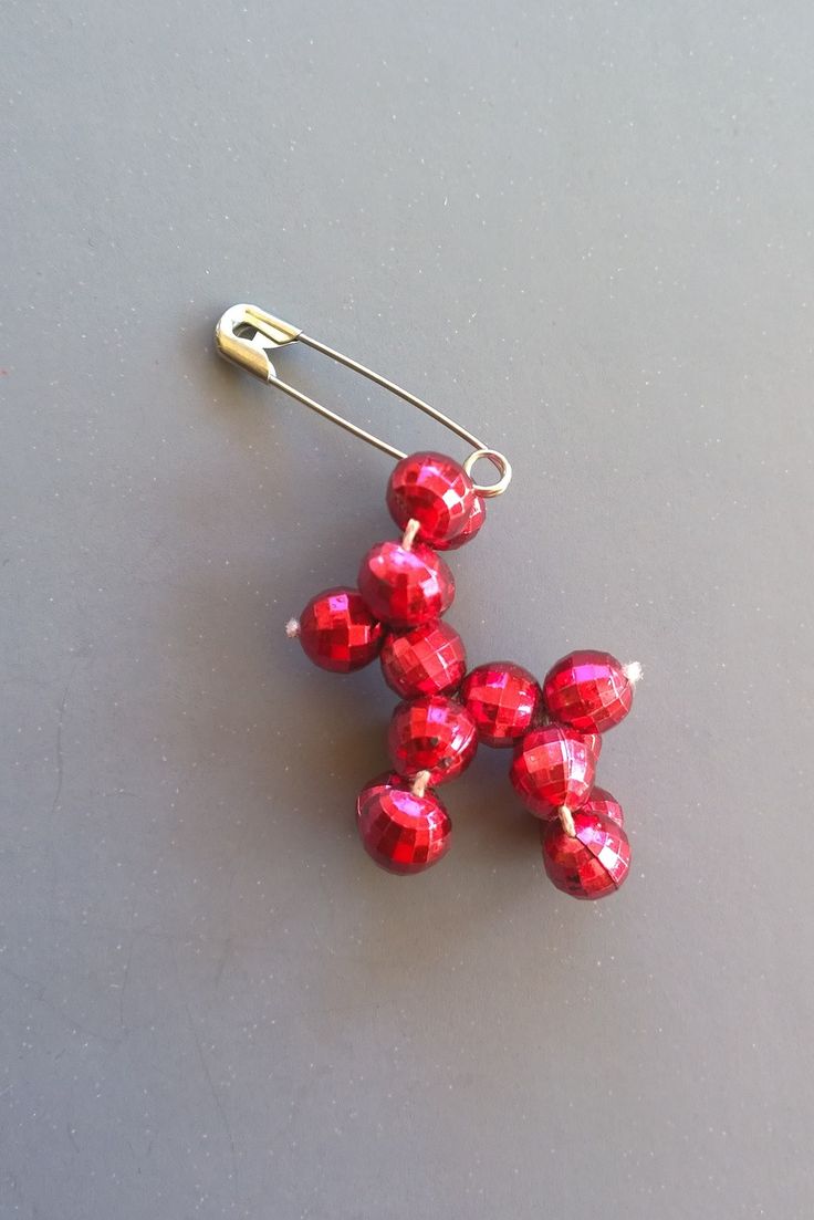 a pair of red beaded earrings sitting on top of a gray surface next to a yellow hook