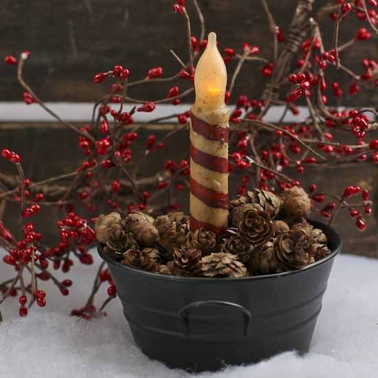 a candle is sitting in a pot filled with pine cones and red berries on the snow