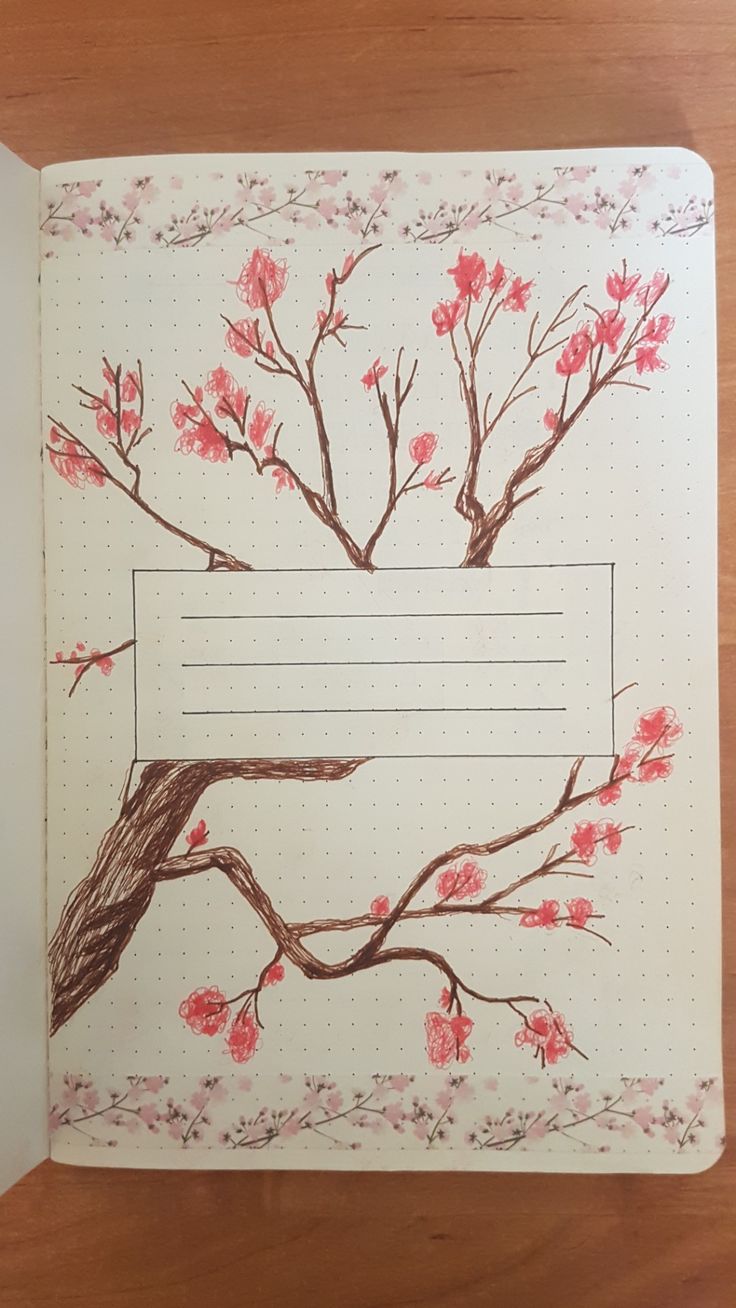 an open notebook with pink flowers and branches drawn on it, sitting on top of a wooden table