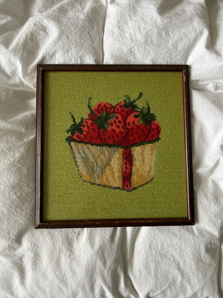 a cross stitch picture of strawberries in a basket on a white sheet with a brown frame