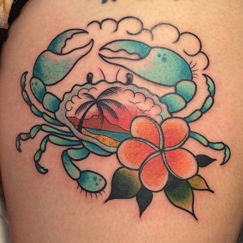 a crab and flower tattoo on the back of a woman's thigh, with an ocean scene in the background