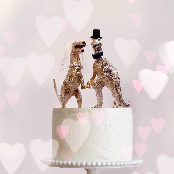 two golden dogs are standing on top of a wedding cake with hearts in the background