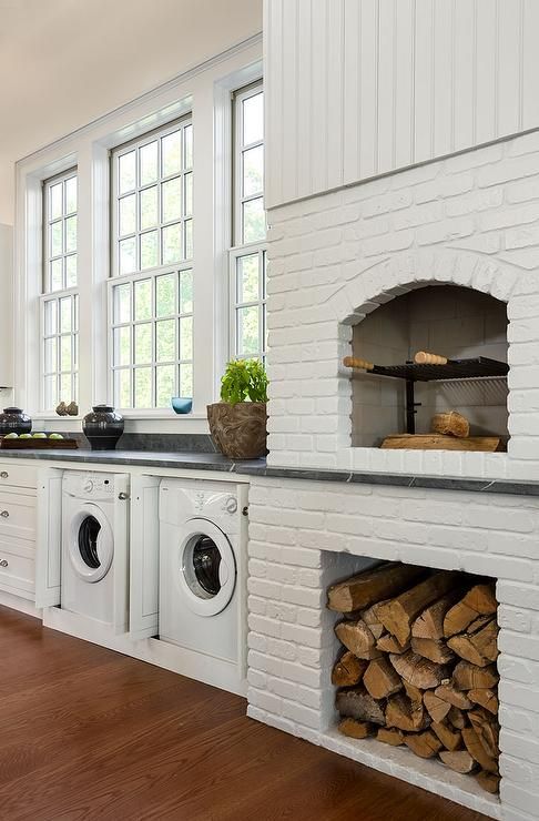 a kitchen with white cabinets and wood stacked on top of each other in front of a brick oven