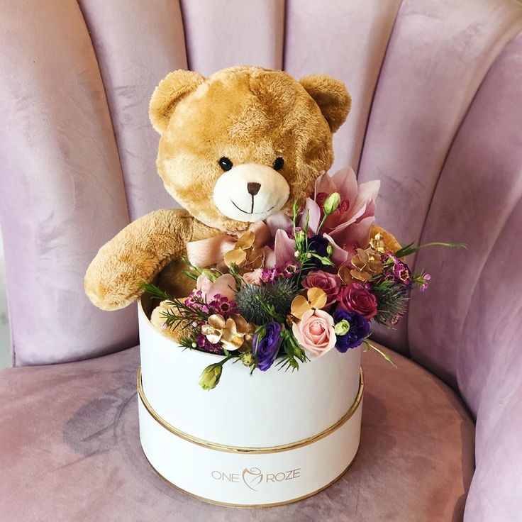 a teddy bear sitting on top of a white box filled with flowers