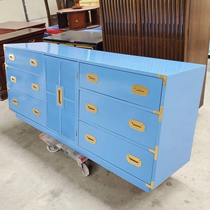 a blue cabinet with gold handles on wheels in a room filled with furniture and other items