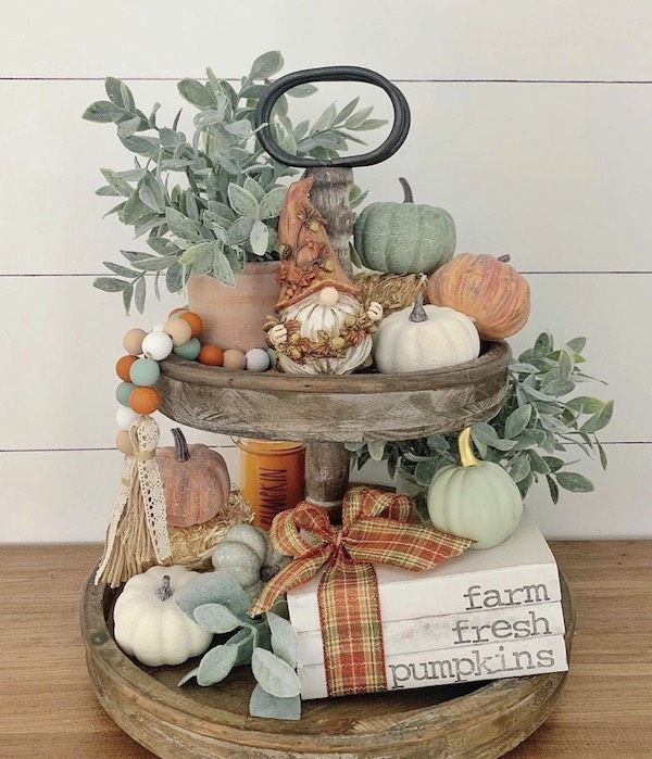 a three tiered tray with pumpkins, gourds and other fall decorations