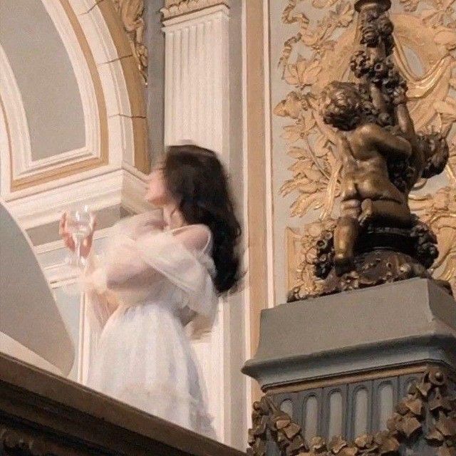 a woman in white dress standing on top of a stair case next to a statue