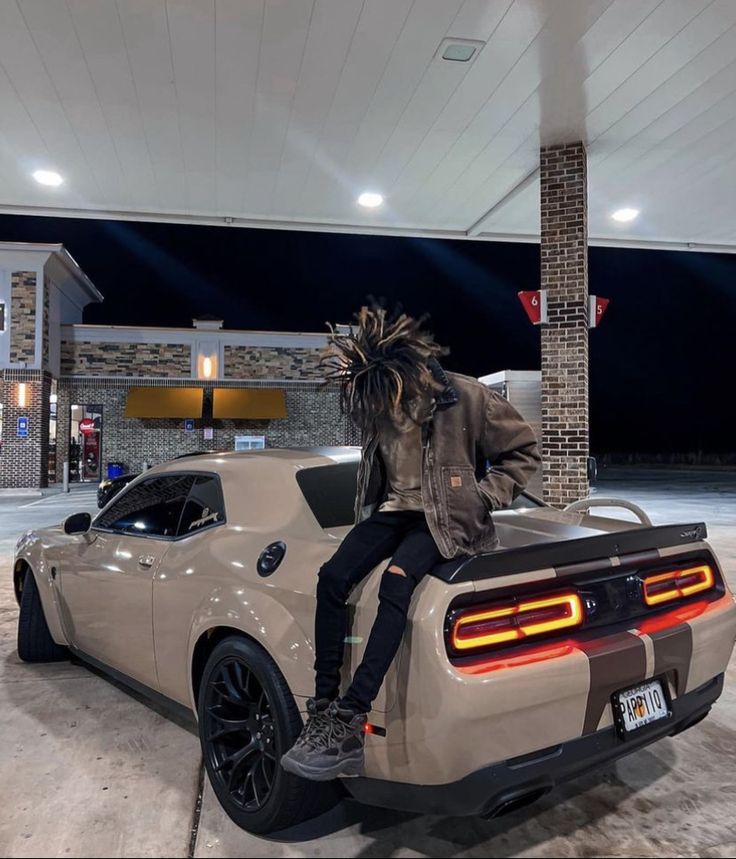 a person sitting on top of a car in a gas station parking lot at night